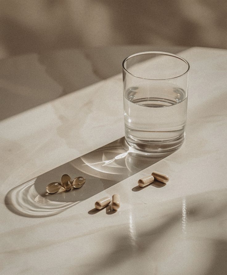 A supplement flat-lay of capsules of Lion Mane and Magnesiumwith a journal and water by Mujer De Conocimiento